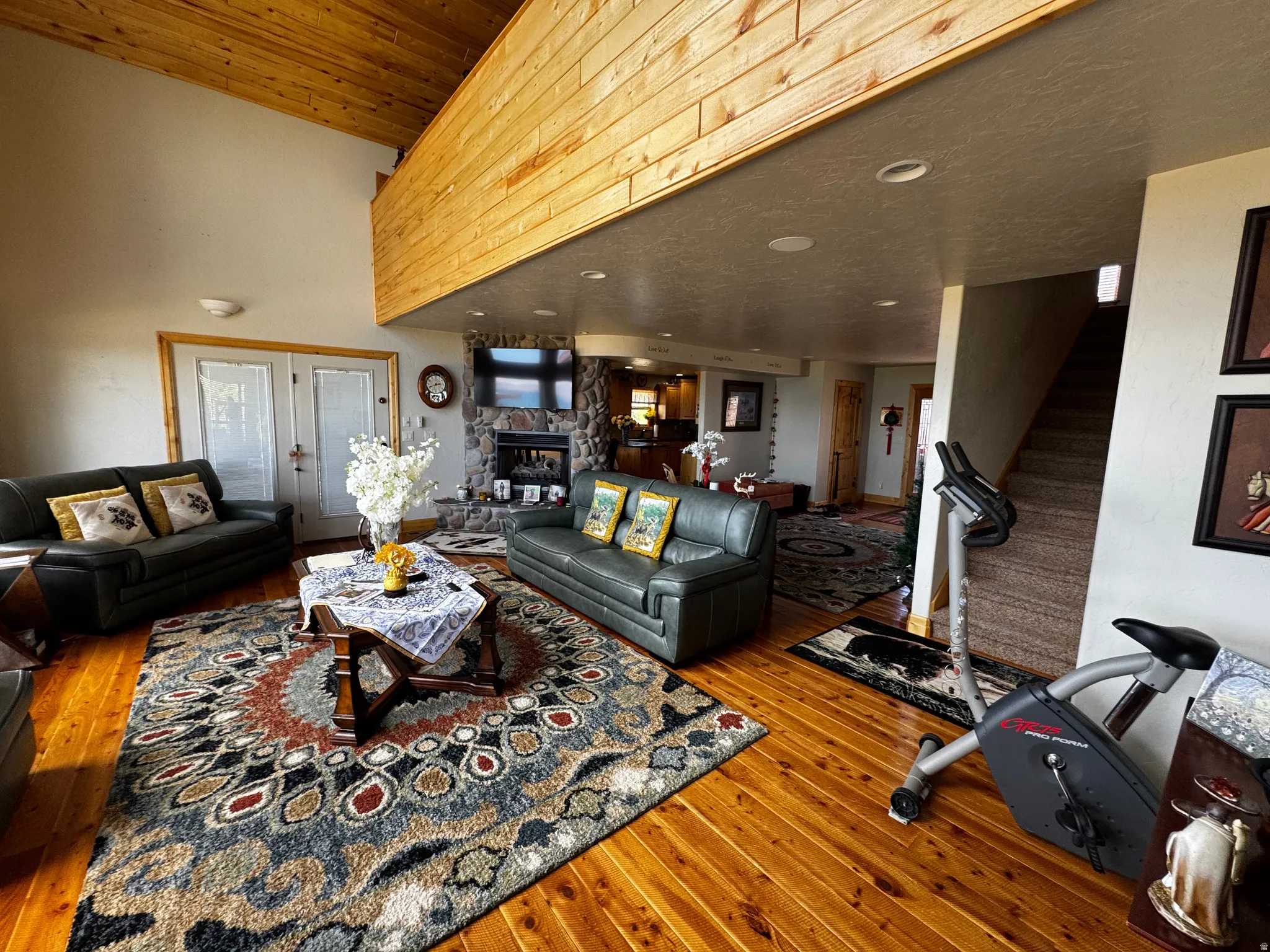 Vaulted wood-paneled ceiling with exposed beams, wood-finish flooring, stone-clad fireplace, recessed lighting, and French doors