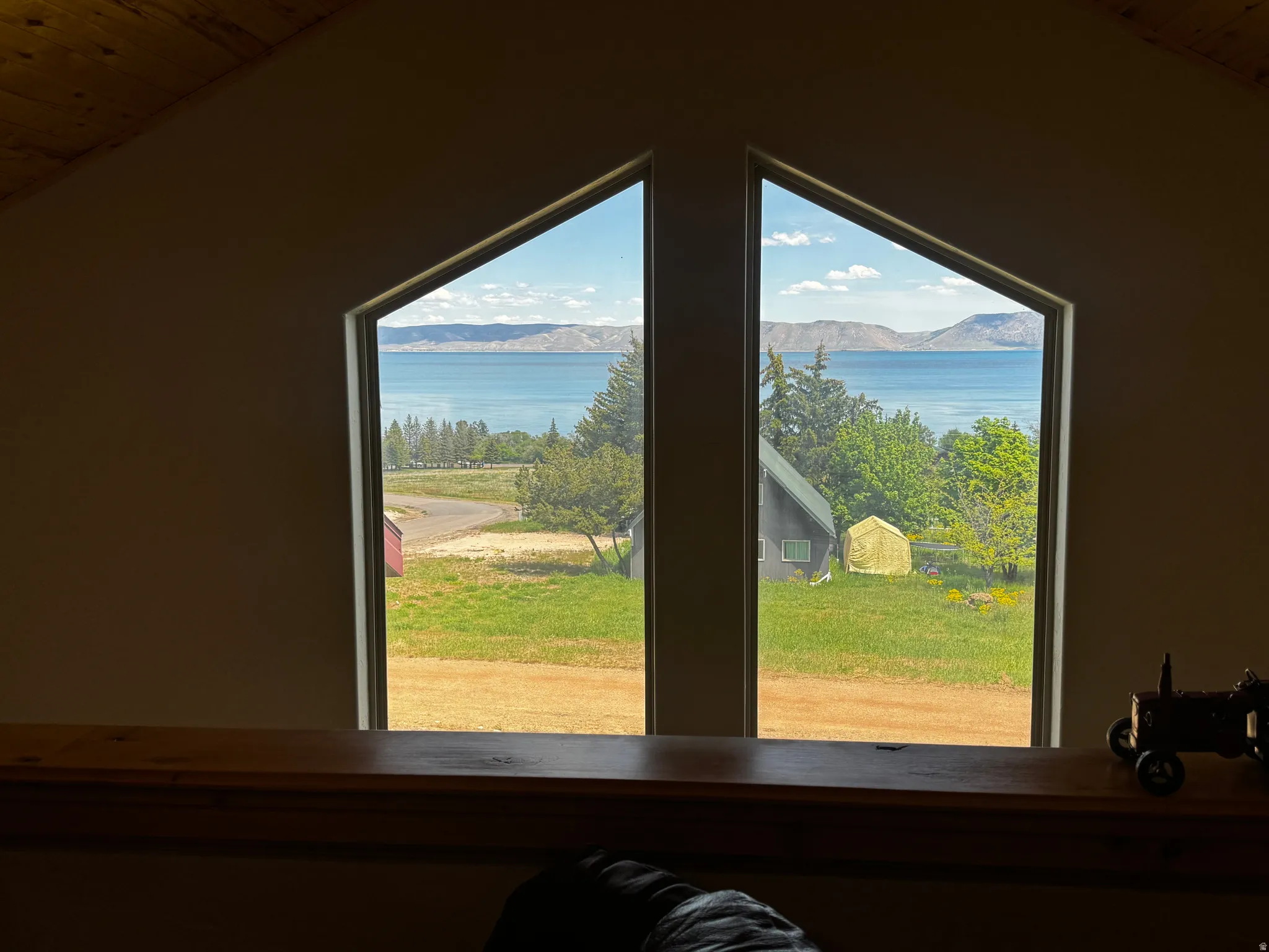 Angled window framing a water body with distant mountains, mature trees, and a grassy expanse