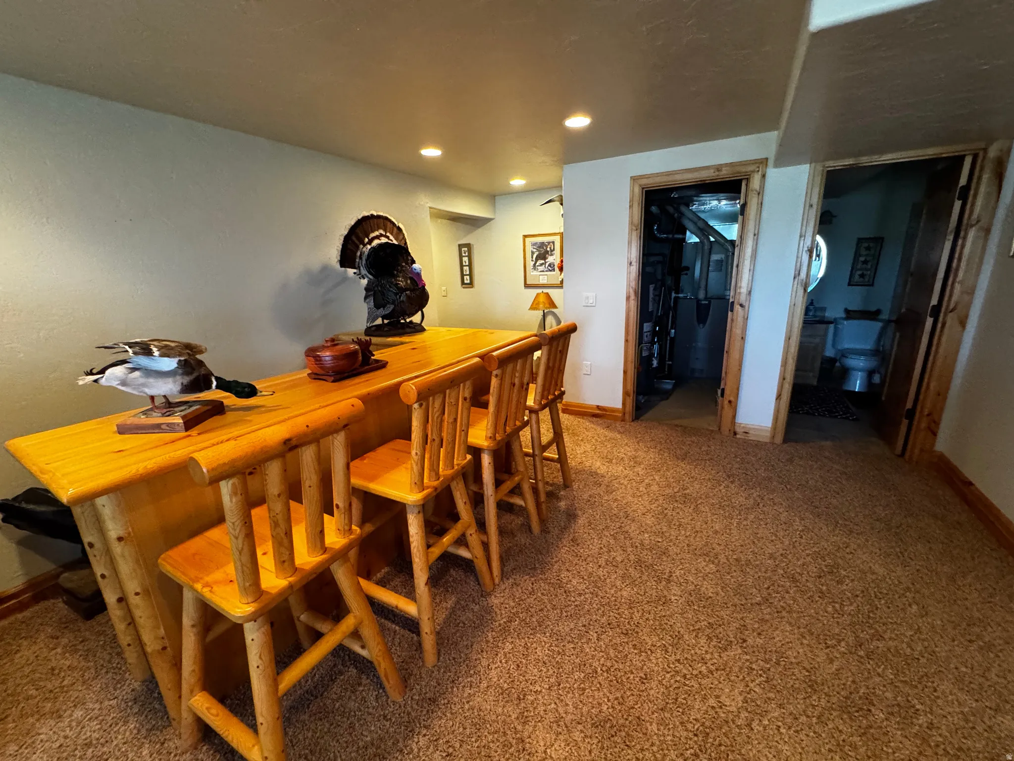 Built-in rustic wood bar with three matching barstools, recessed lighting, and carpeted flooring