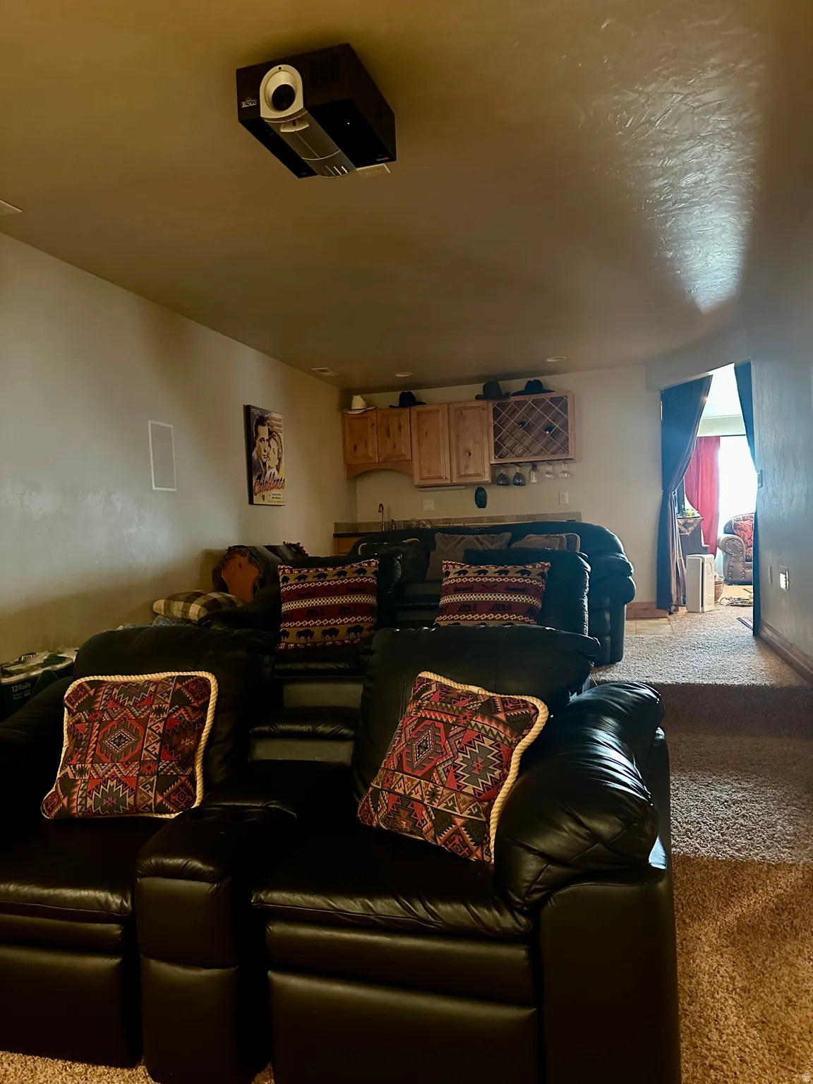 Dedicated media room featuring tiered seating, built-in projector, integrated speakers, and a wet bar with wood cabinetry
