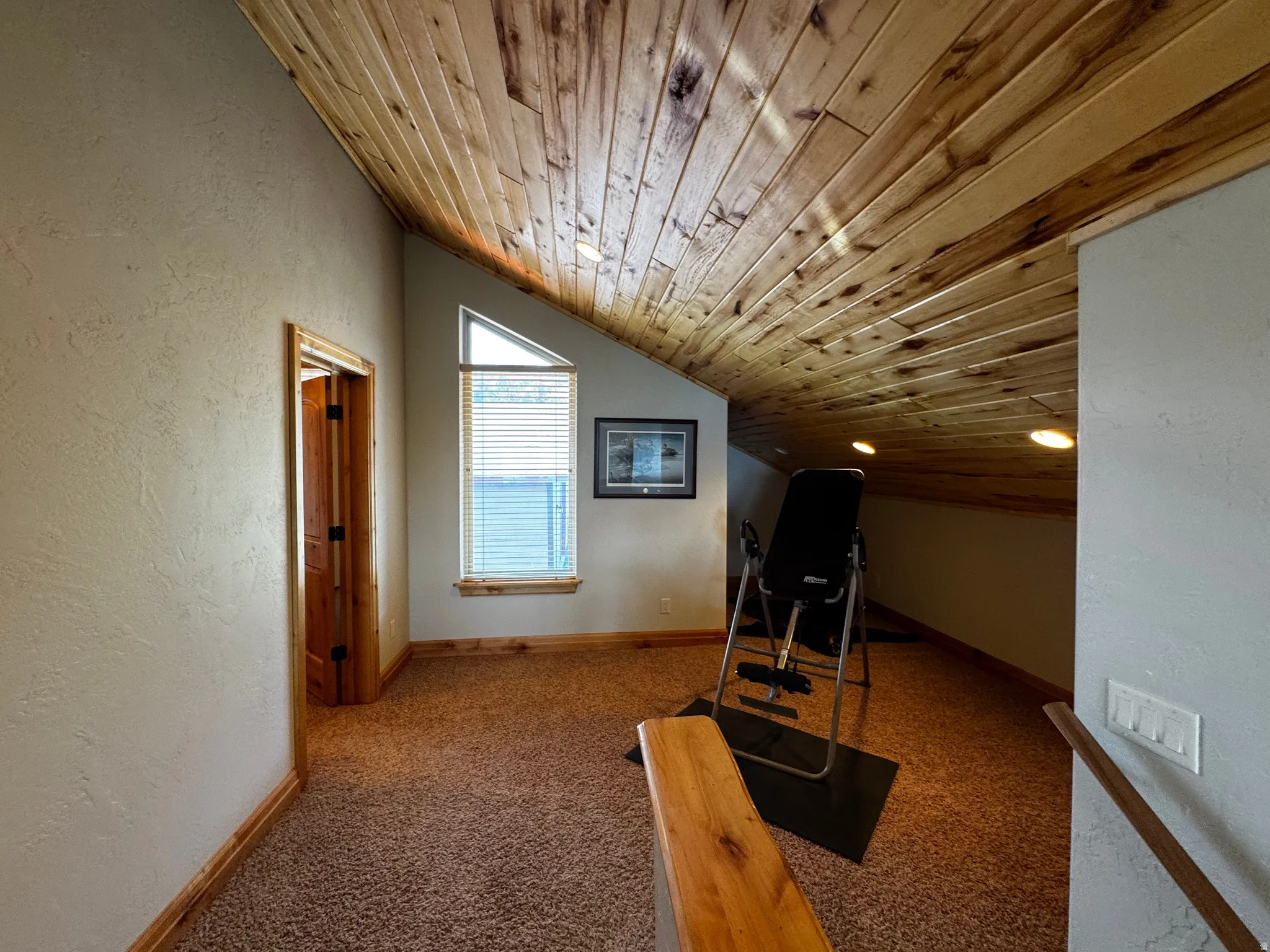 Carpeted loft area featuring a vaulted wood-paneled ceiling with recessed lighting, a triangular window with blinds, and wood trim detailing