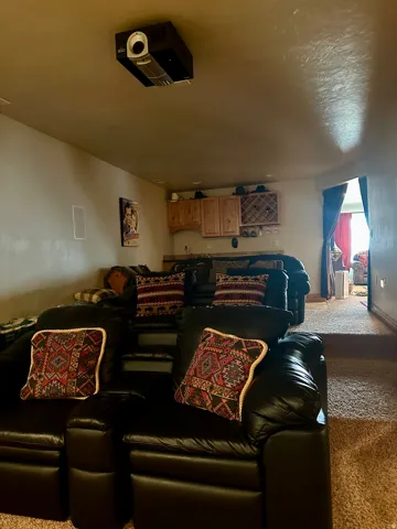 Dedicated media room featuring tiered seating, built-in projector, integrated speakers, and a wet bar with wood cabinetry