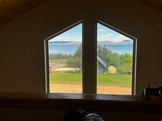 Angled window framing a water body with distant mountains, mature trees, and a grassy expanse