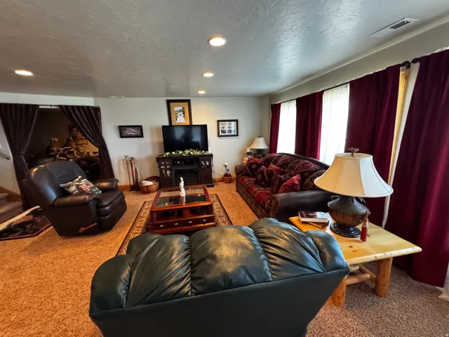 Carpeted living area featuring recessed ceiling lighting, a built-in media console with an electric fireplace, and multiple windows dressed with full-length drapery
