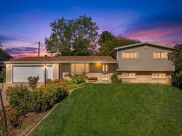 Split-level residence featuring a two-car garage, brick and siding exterior, and a manicured front lawn with established landscaping