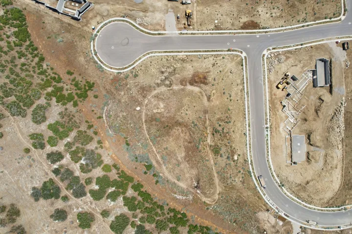 Aerial perspective of a developing residential area featuring paved streets, a cul-de-sac, and undeveloped land with natural vegetation
