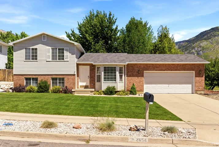 Split-level residence featuring a brick facade, light-colored siding, and a two-car garage