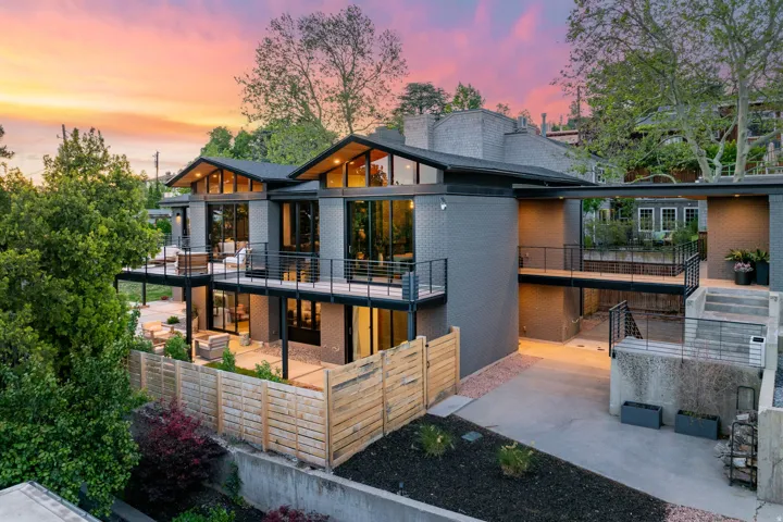 Multi-level contemporary residence featuring extensive glazing, multiple outdoor balconies, a private patio, and a concrete driveway