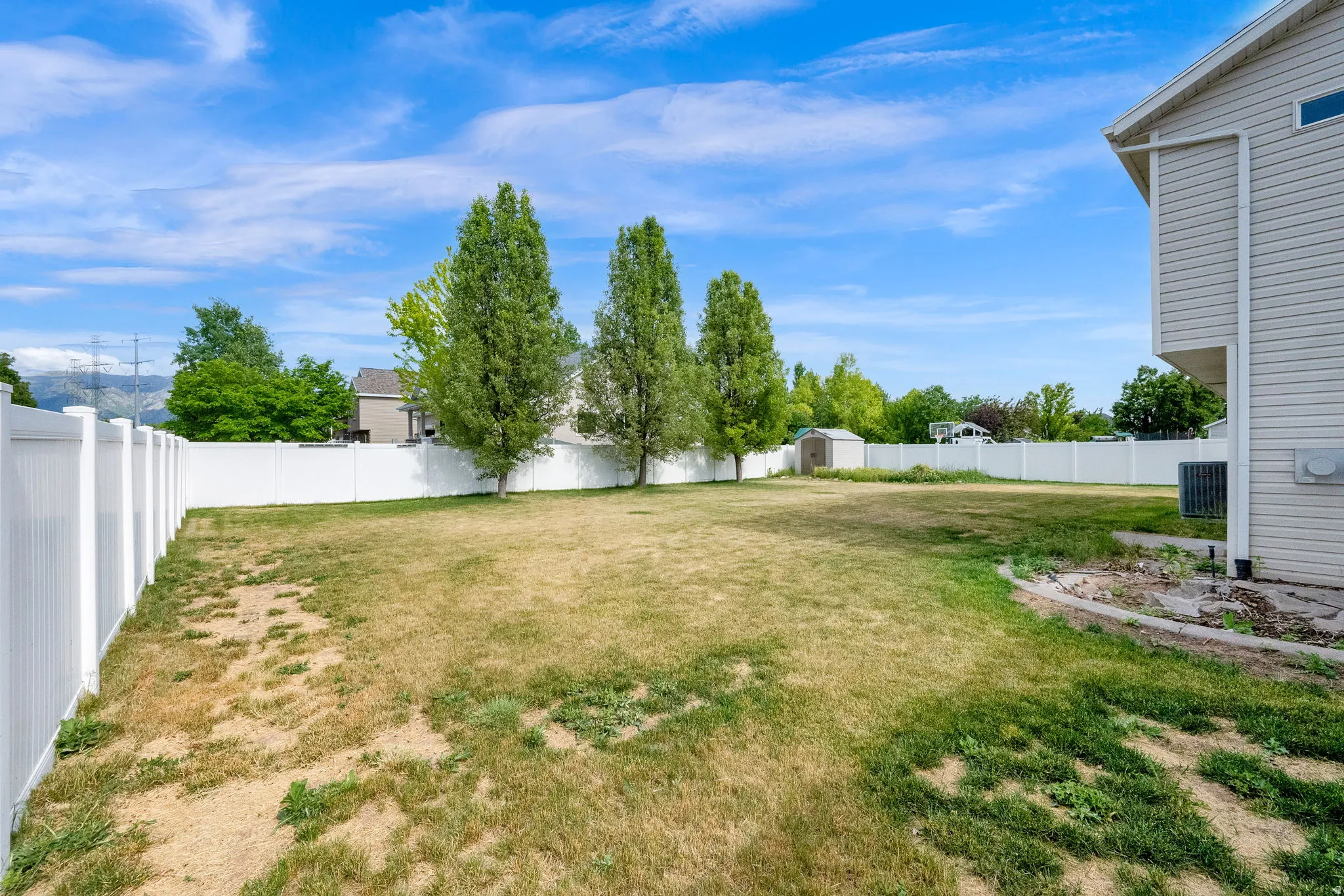 Expansive yard enclosed by a white privacy fence, featuring mature trees and a detached shed