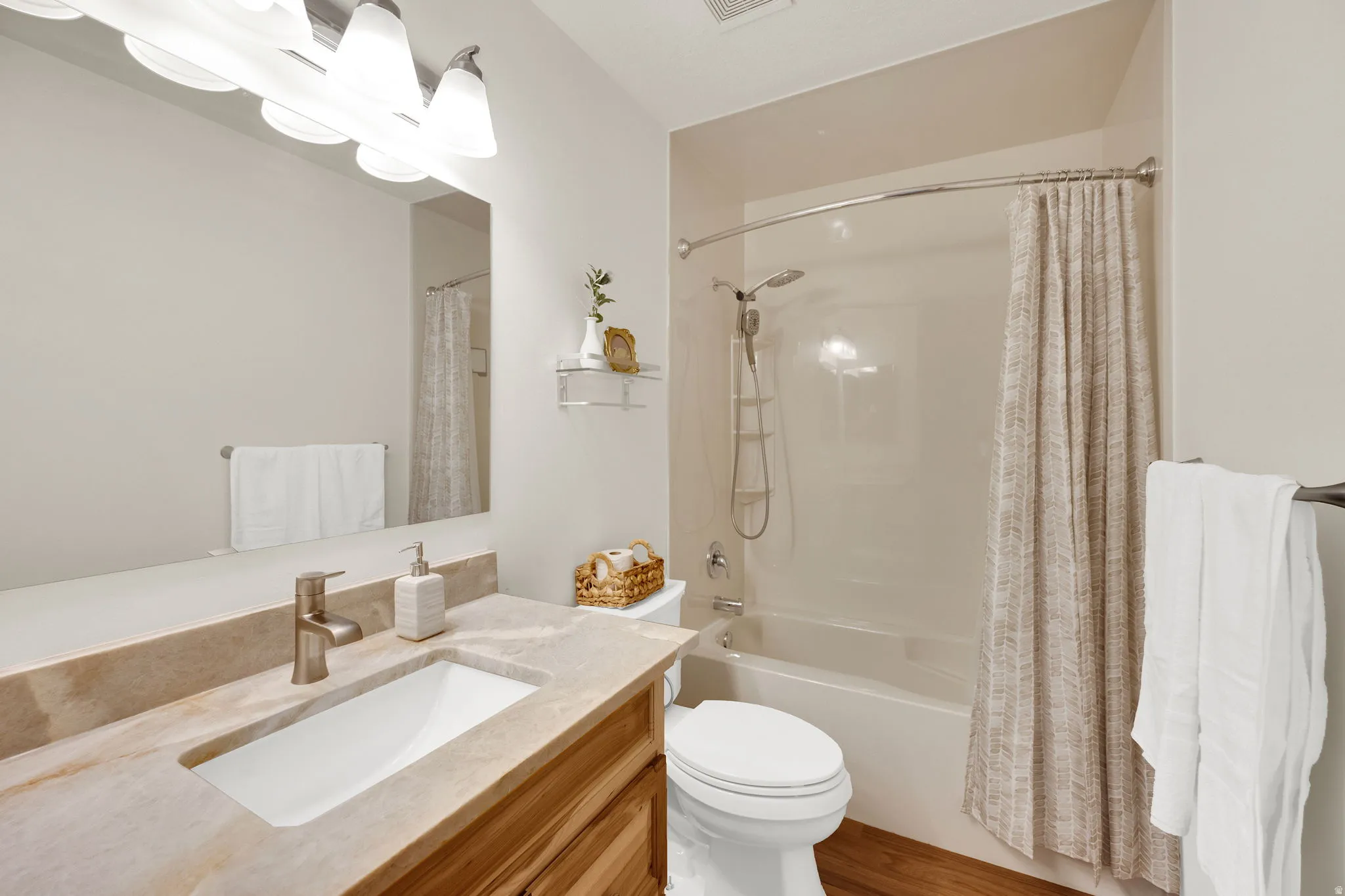 Full bathroom featuring a single vanity with an undermount sink, a light-toned countertop, a large wall-mounted mirror, a tub/shower combination, and wood-finish flooring