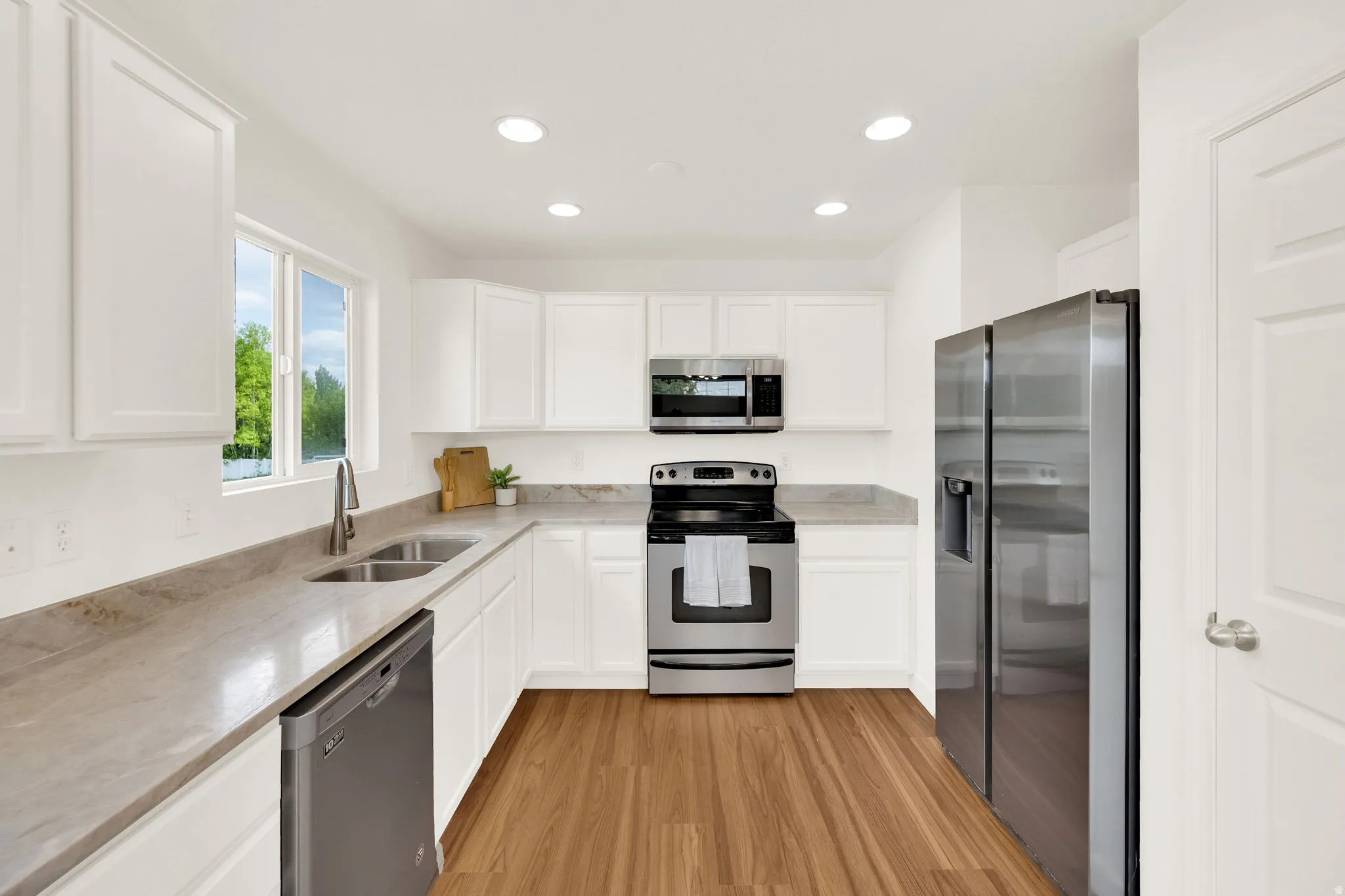 Bright kitchen featuring white cabinetry, light-toned countertops, and wood-finish flooring