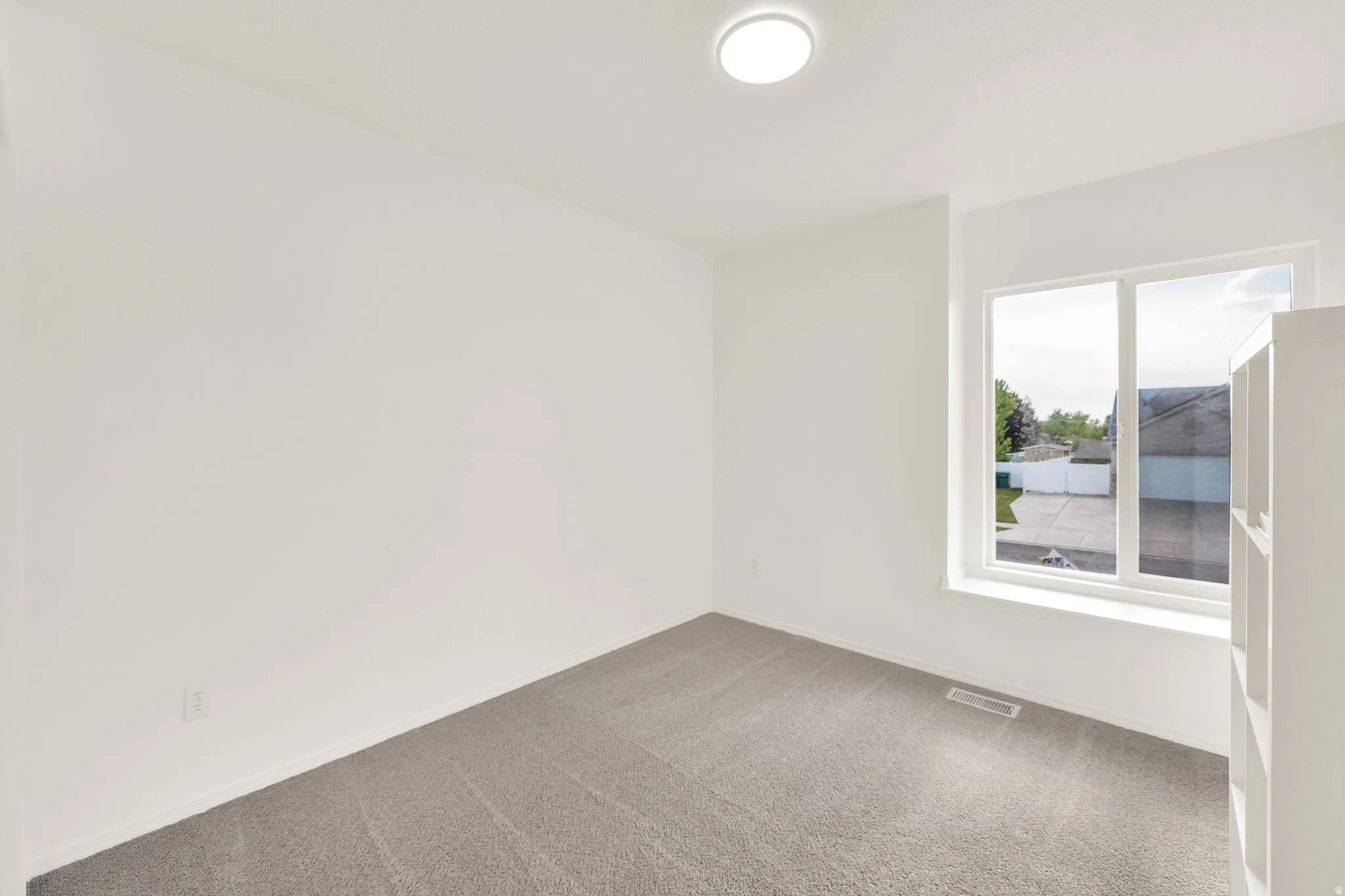 Bright room featuring light gray carpet flooring, white walls, and a large window with white framing