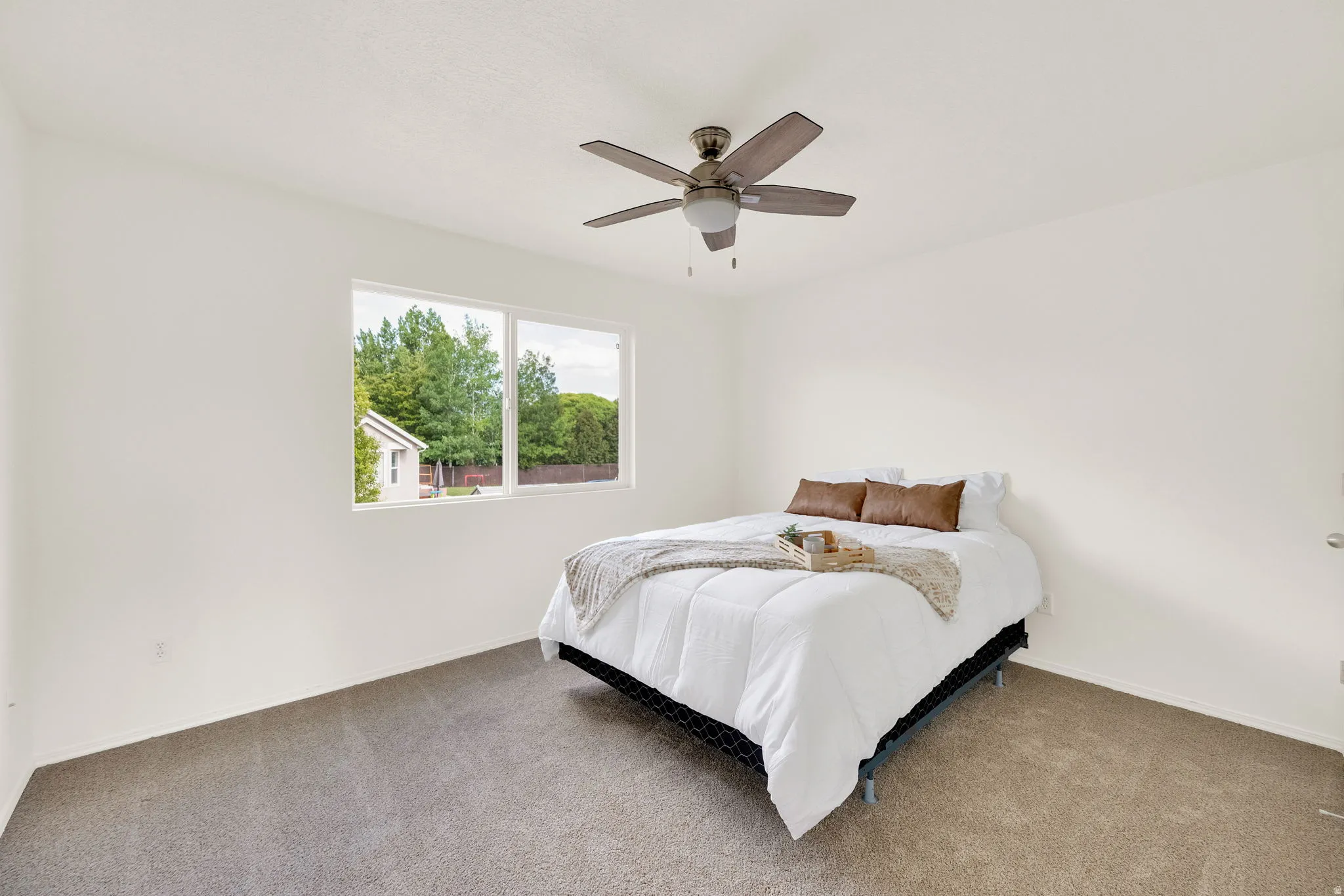 Spacious room featuring neutral carpeting, white wall finishes, a multi-pane window, and a ceiling fan with integrated lighting