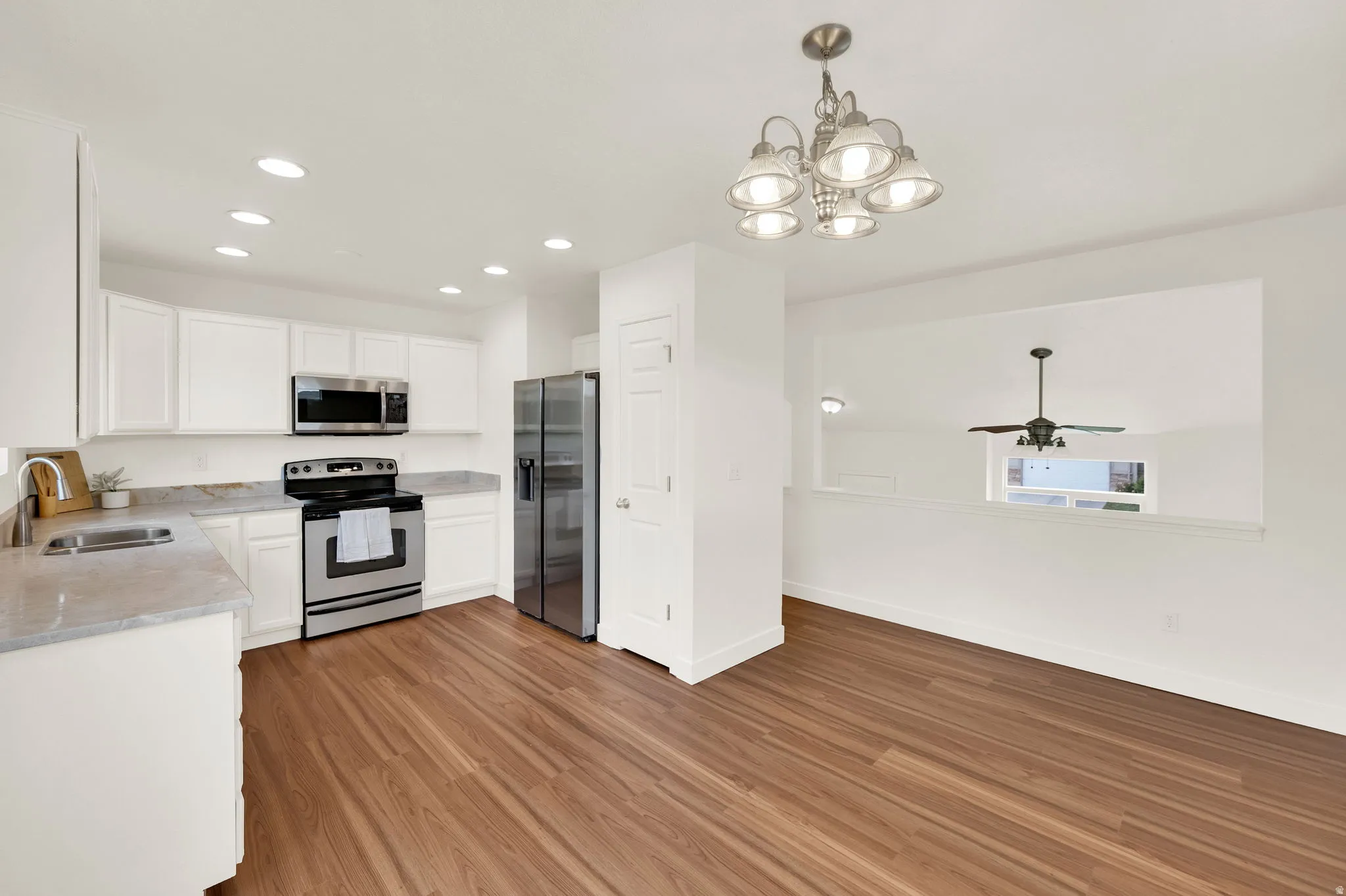 Open-concept kitchen and dining area featuring wood-finish flooring, white cabinetry, stainless steel appliances, and a modern chandelier