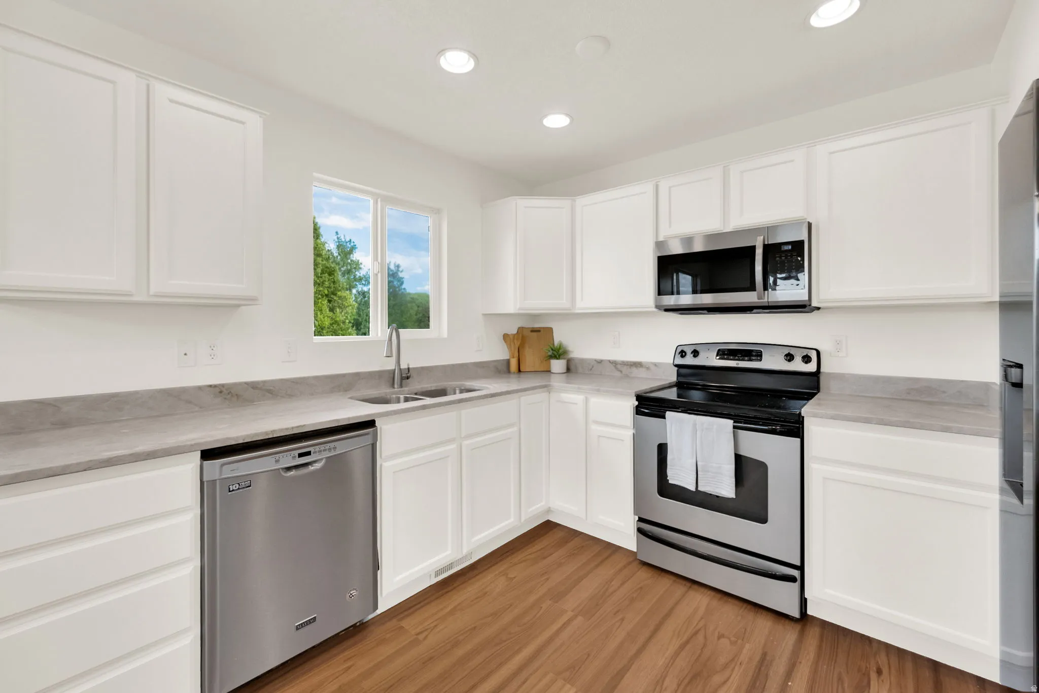 Kitchen featuring white shaker-style cabinetry, stainless steel appliances, grey stone-finish countertops, wood-finish flooring, and recessed lighting