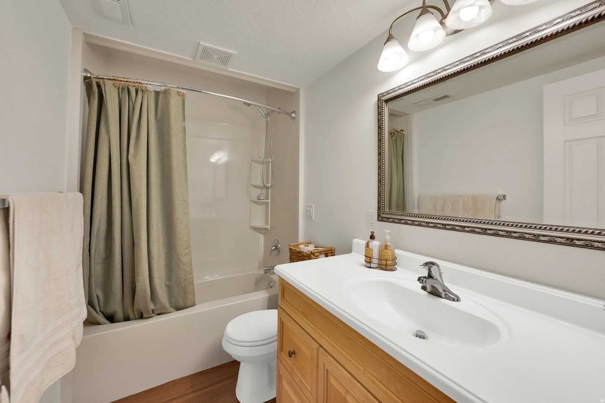 Bathroom featuring a wood-finish vanity with an integrated white sink, a decorative framed mirror, and a full bathtub with a shower kit