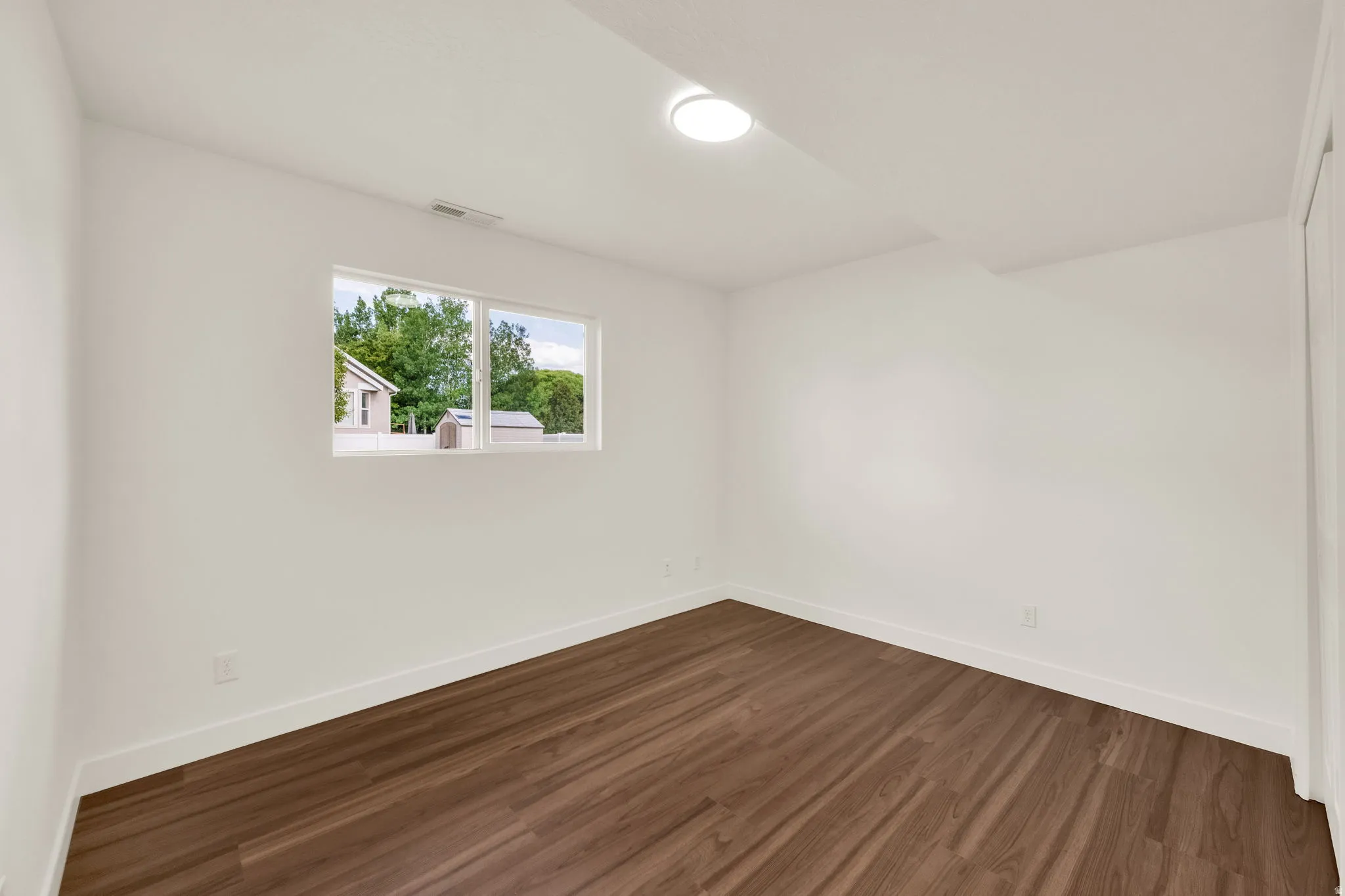 Room featuring wood-finish flooring, white walls, and a window with white trim