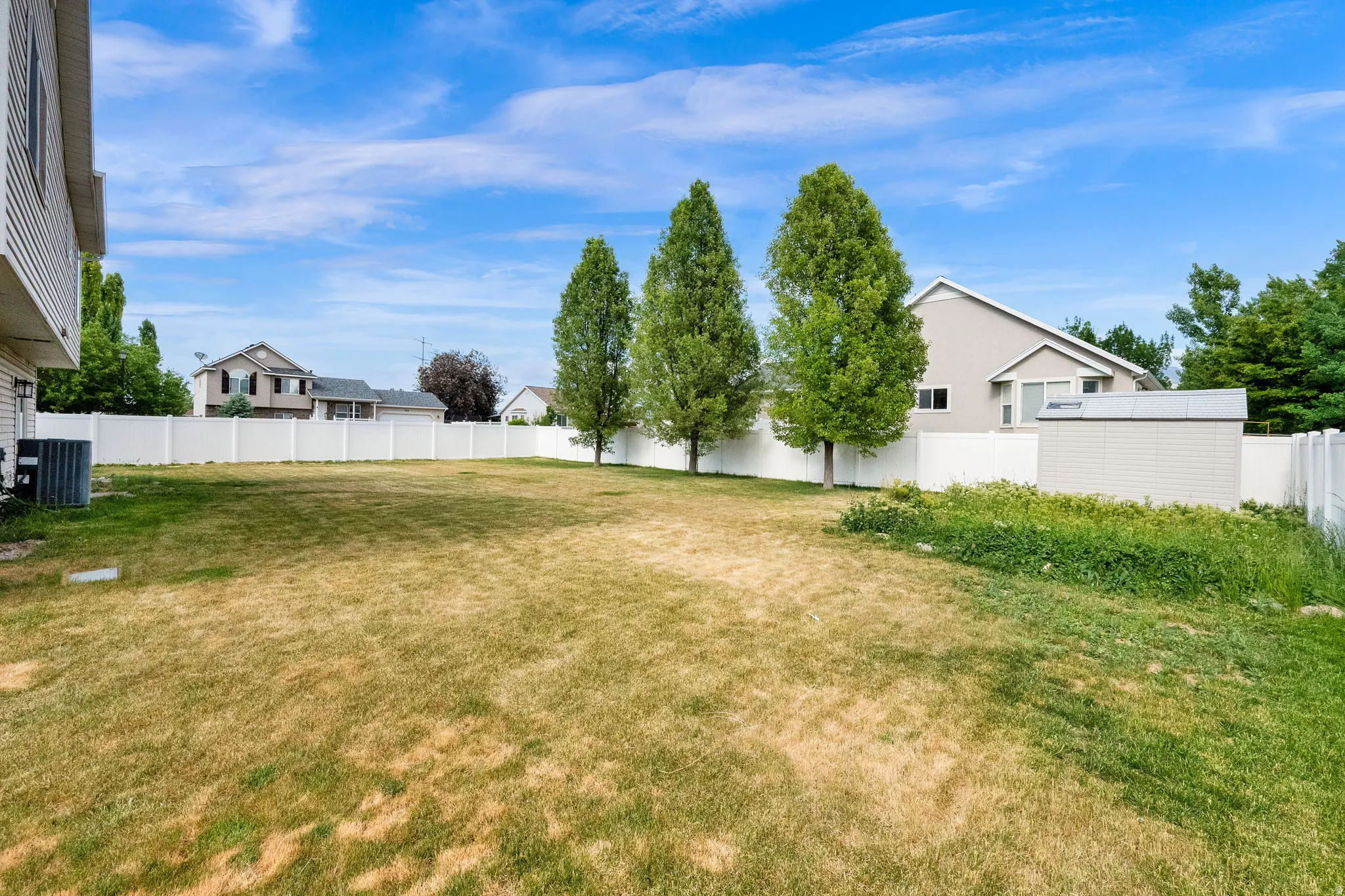 Spacious backyard featuring a perimeter privacy fence, mature trees, and a detached storage shed