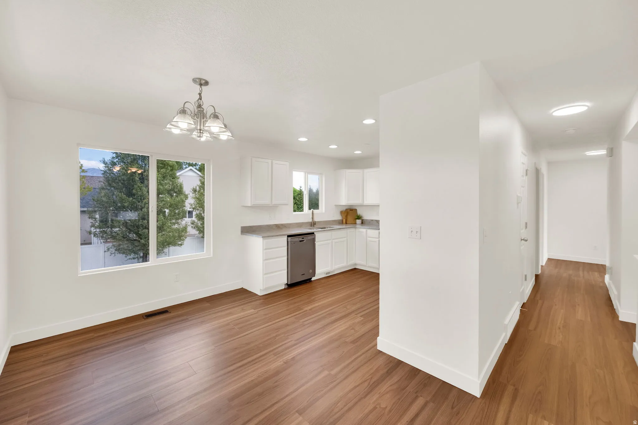 Open-concept living space with wood-finish flooring, a contemporary chandelier, and a bright window