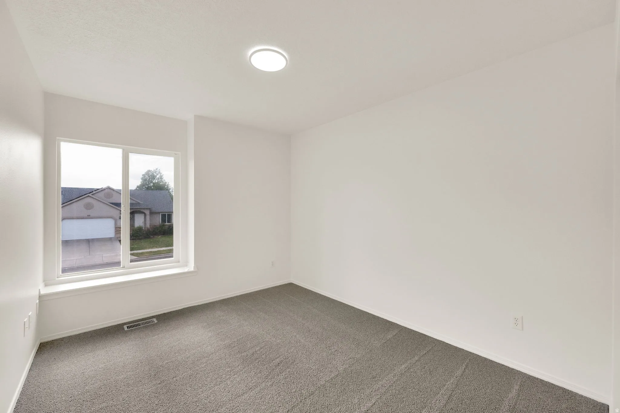 Bright interior space featuring a large window with white trim, neutral wall tones, and gray carpeting