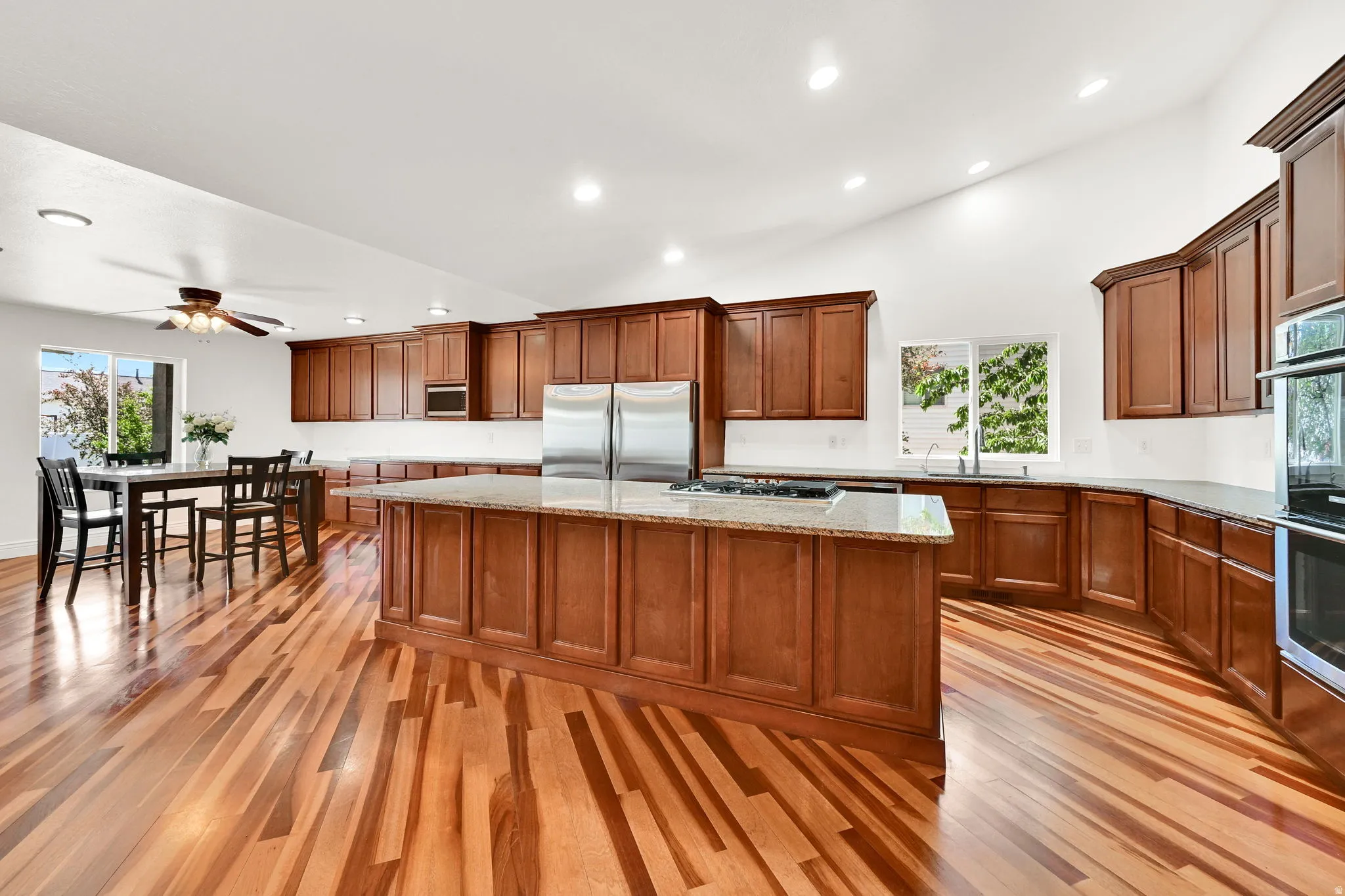 Spacious kitchen featuring extensive wood-finish flooring, a large central island with a granite countertop, and ample wood cabinetry