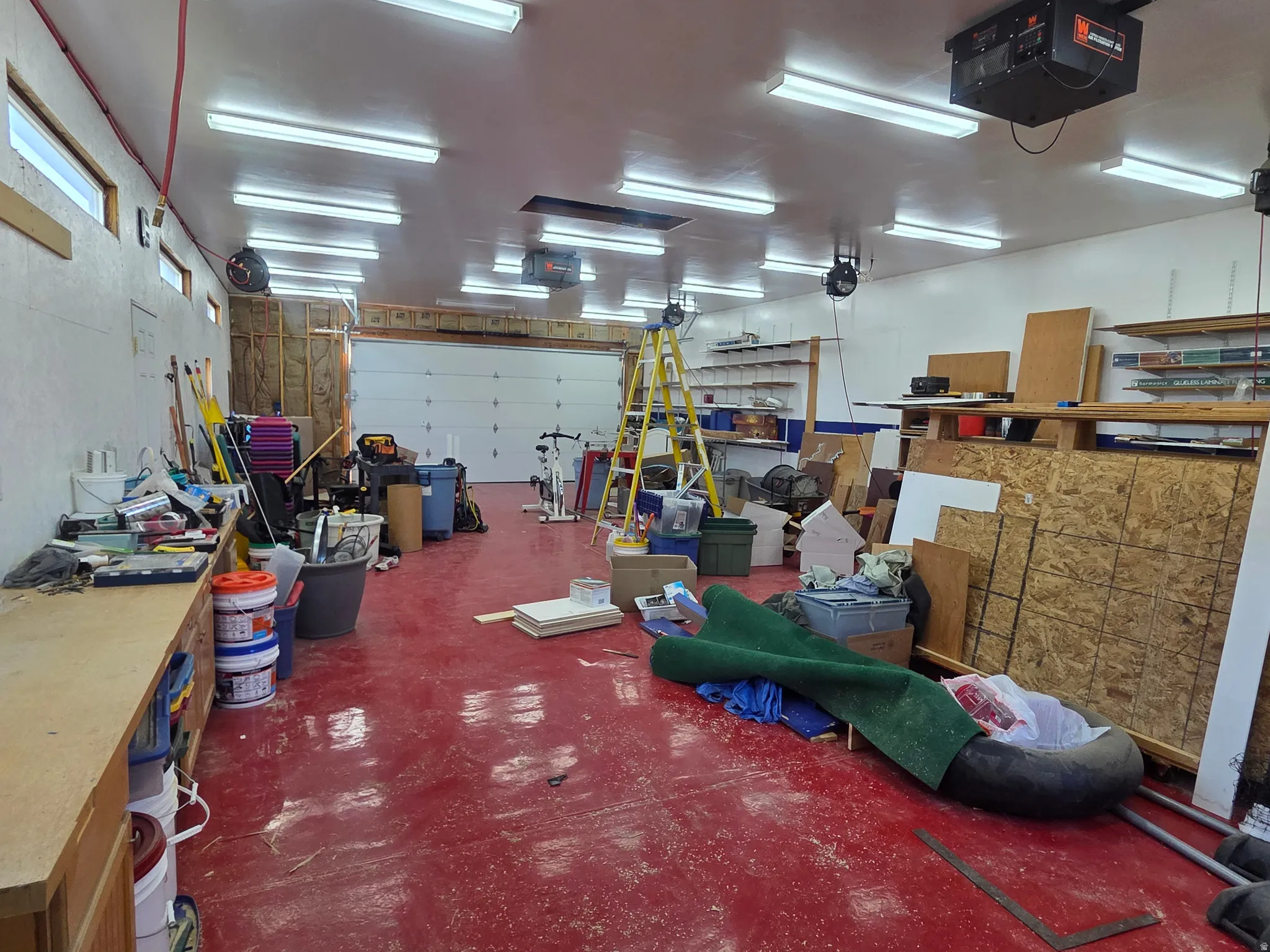 Spacious garage with a red-painted concrete floor and ample overhead fluorescent lighting