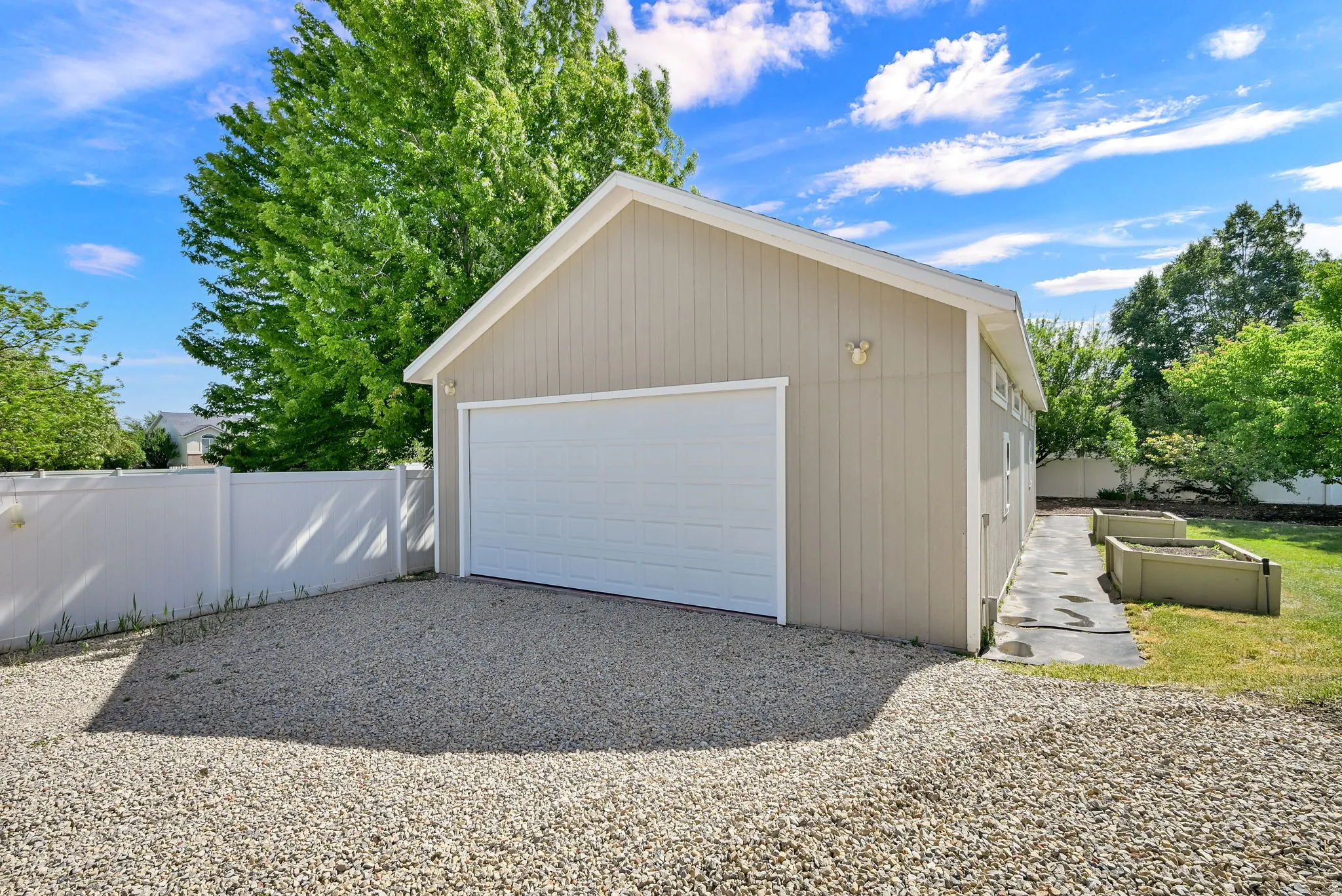 Detached garage structure with a white panel garage door, tan vertical siding, and a white vinyl privacy fence