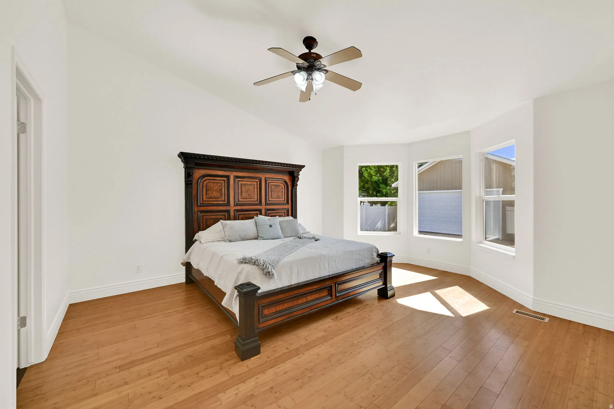 Spacious room featuring vaulted ceilings, wood-finish flooring, a ceiling fan with integrated lighting, and a bay window configuration with multiple windows
