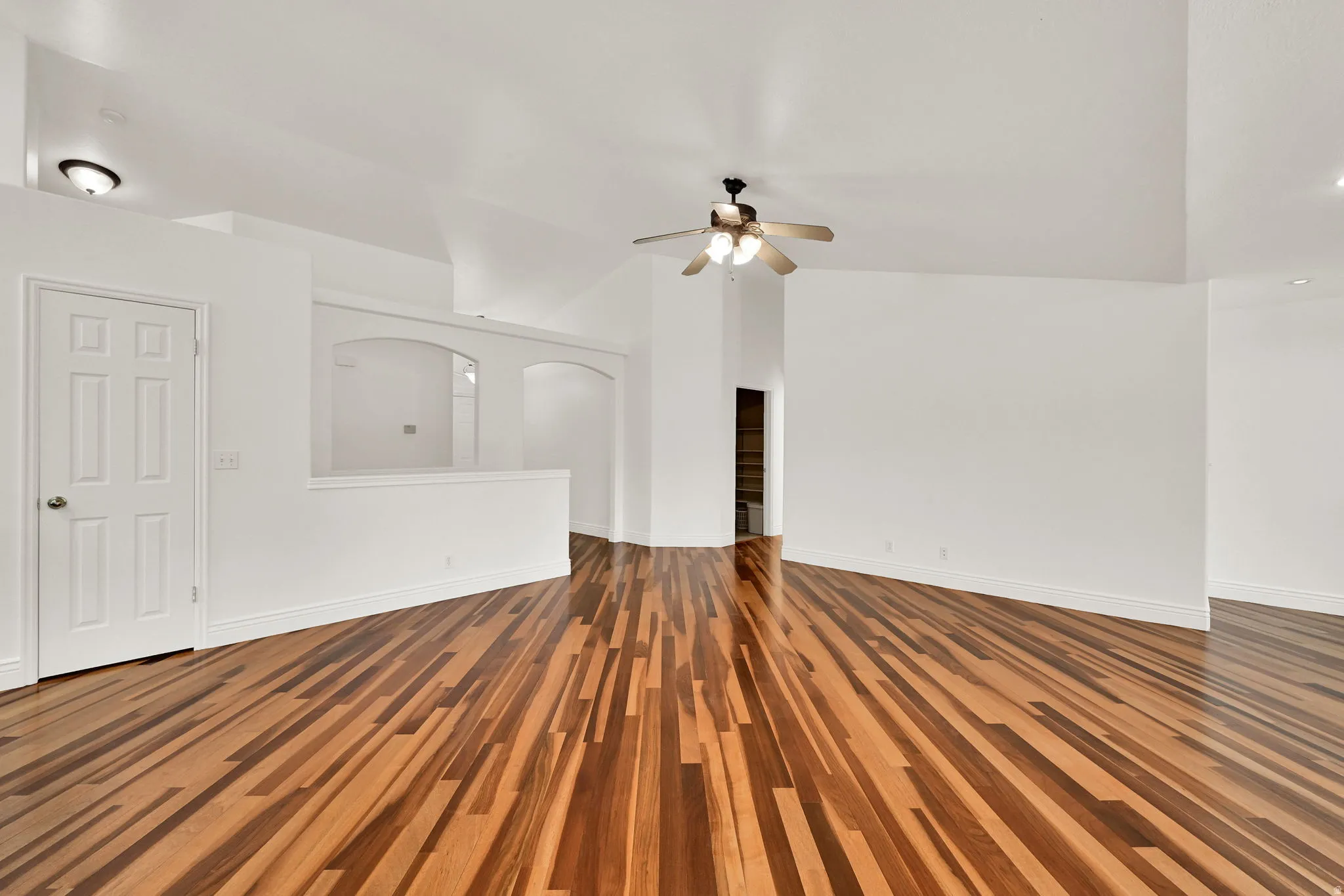 Spacious interior featuring wood-finish flooring, vaulted ceilings, a ceiling fan, arched wall cutouts, and white baseboards