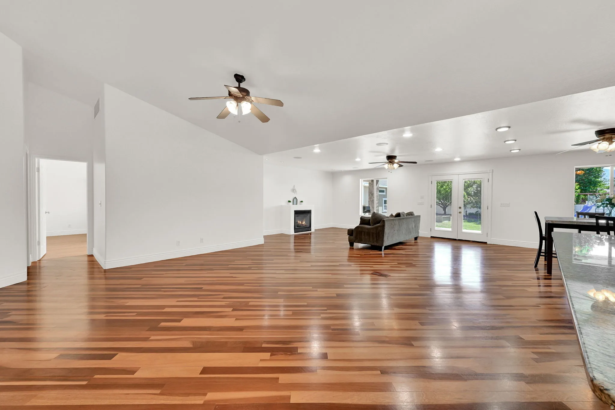 Spacious living area featuring warm wood-finish flooring, white walls, and a vaulted ceiling