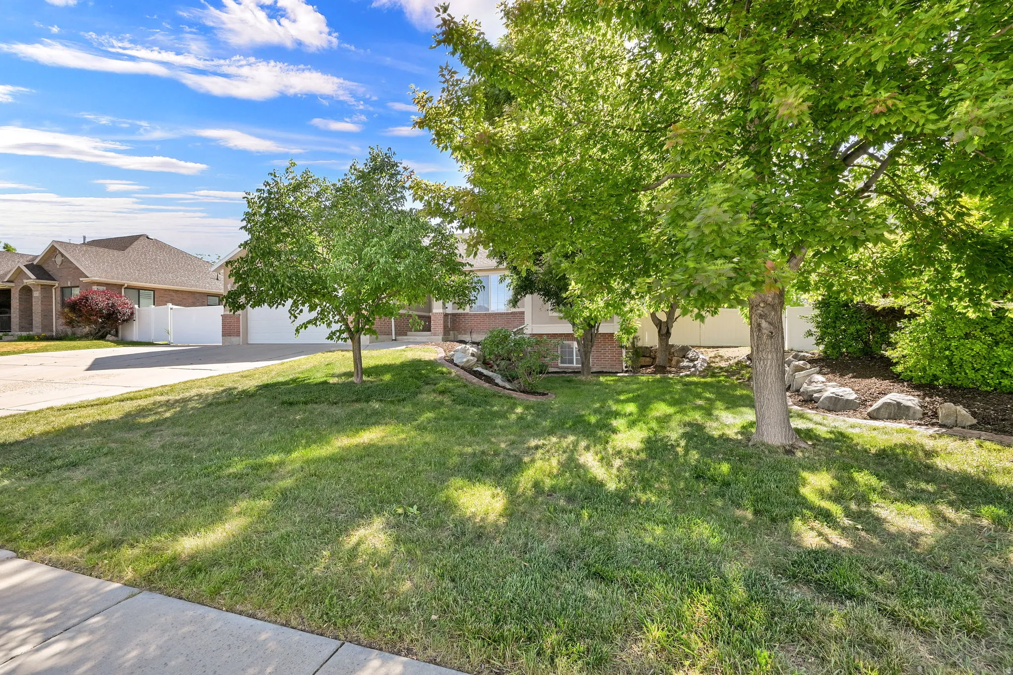 Front yard featuring mature trees, landscaped rock beds, and a manicured lawn
