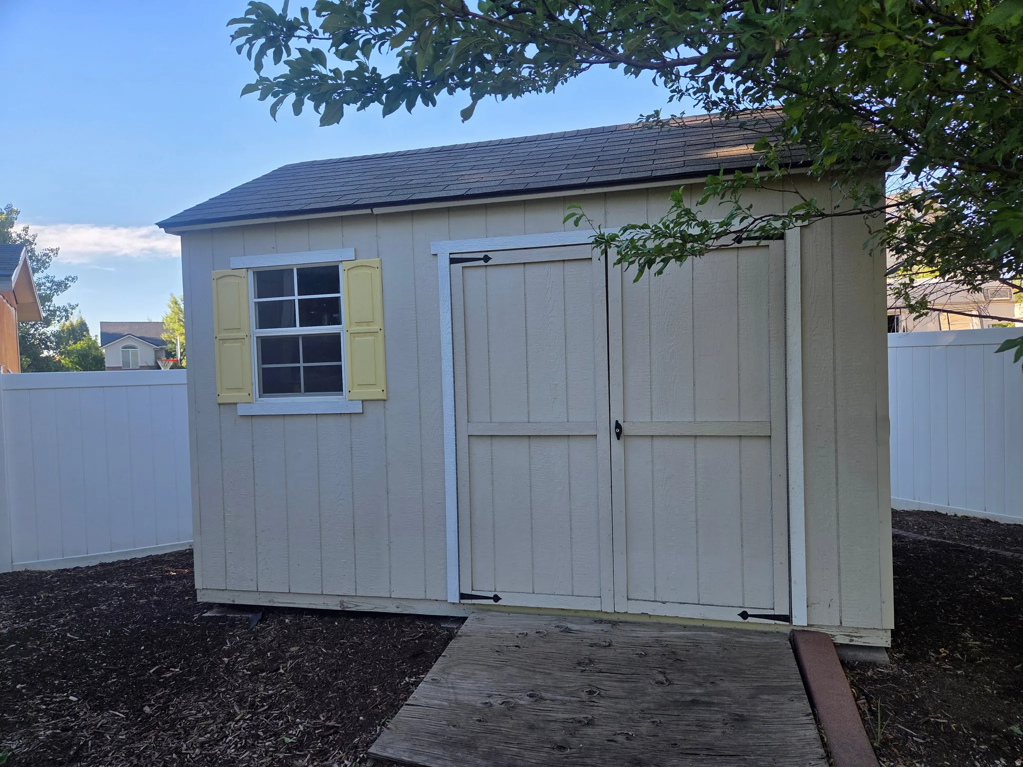 Detached shed featuring a shingled roof, double barn doors, a multi-pane window with decorative yellow shutters, and a slatted wood ramp