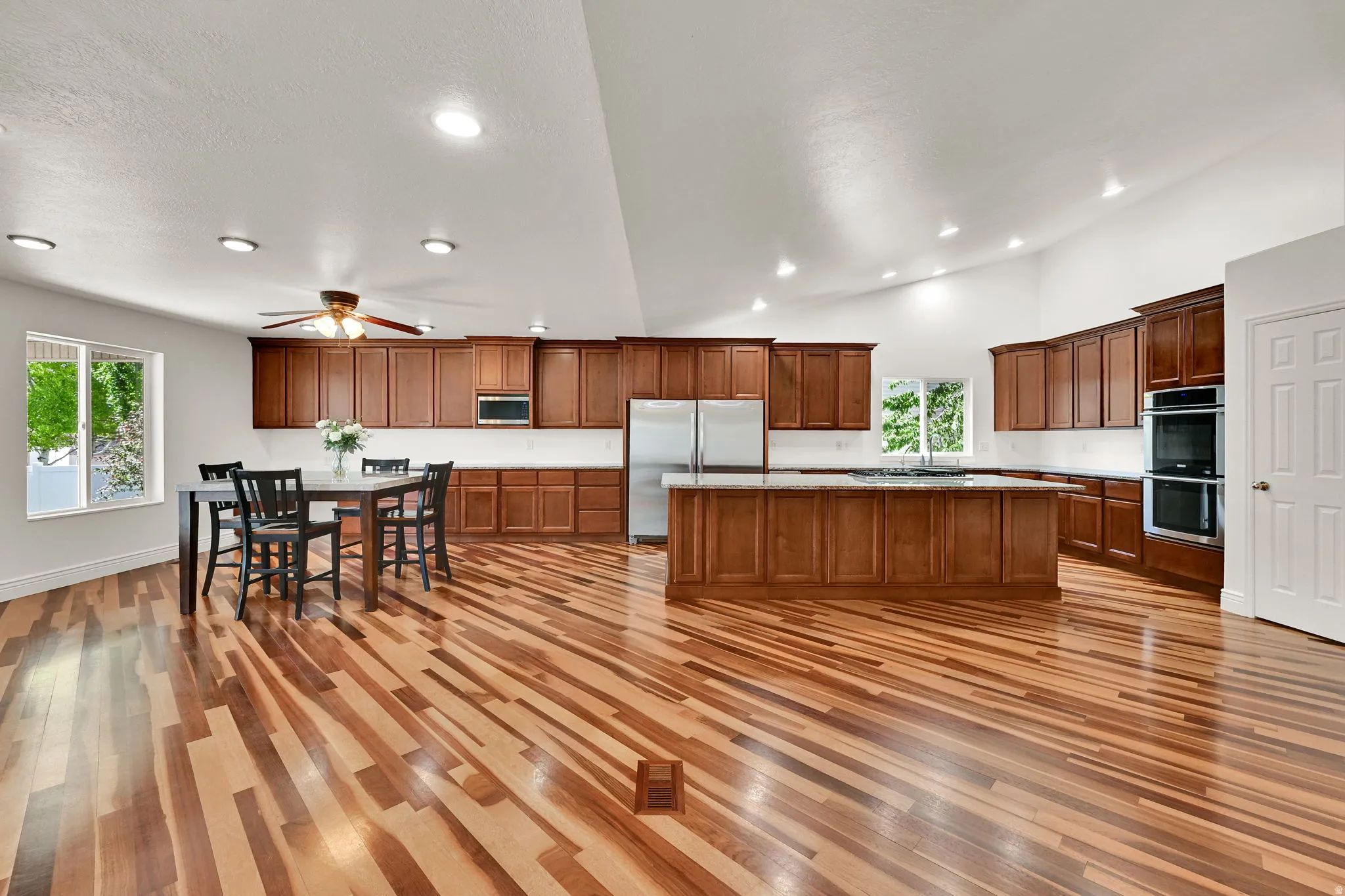 Spacious kitchen and dining area featuring vaulted ceilings, wood-finish flooring, abundant wood cabinetry, stainless steel appliances, and an expansive island