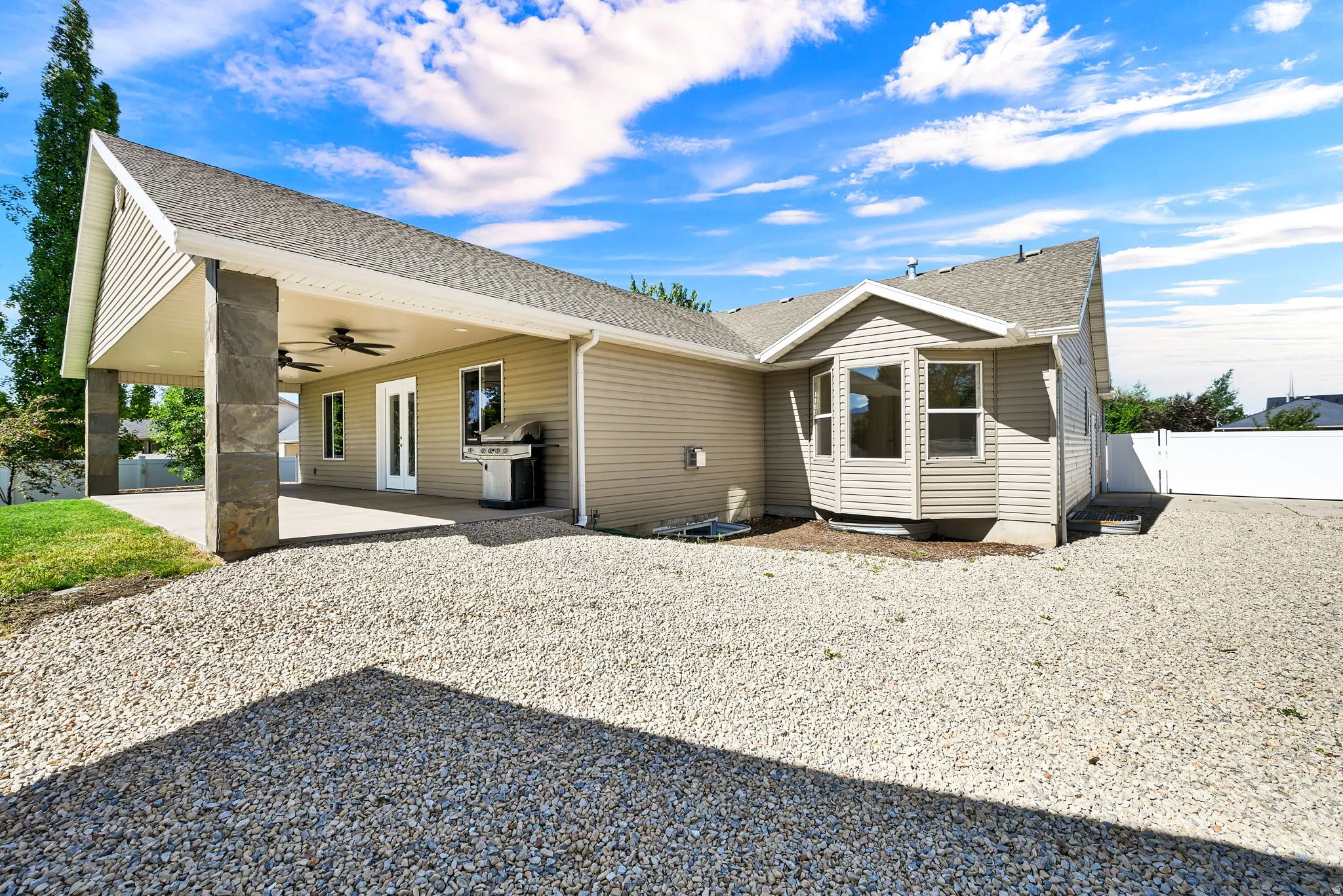 Expansive covered patio with concrete flooring, stone-clad columns, and dual ceiling fans