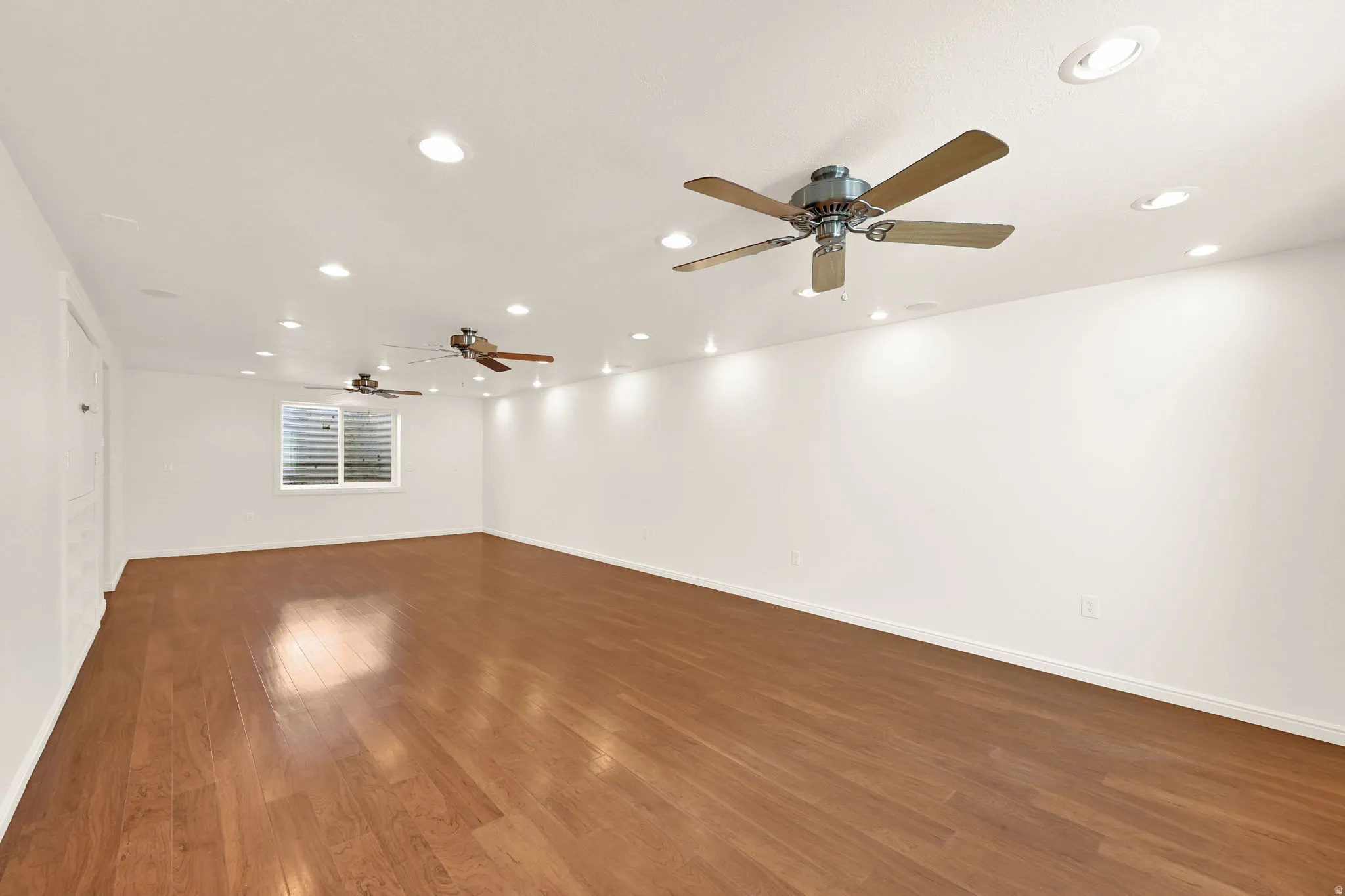 Spacious room featuring wood-finish flooring, recessed lighting, and multiple ceiling fans for air circulation