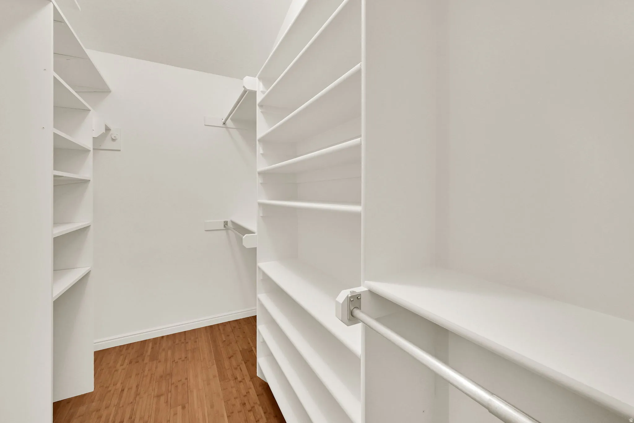 Walk-in closet featuring extensive white shelving, multiple hanging rods, and wood-finish flooring