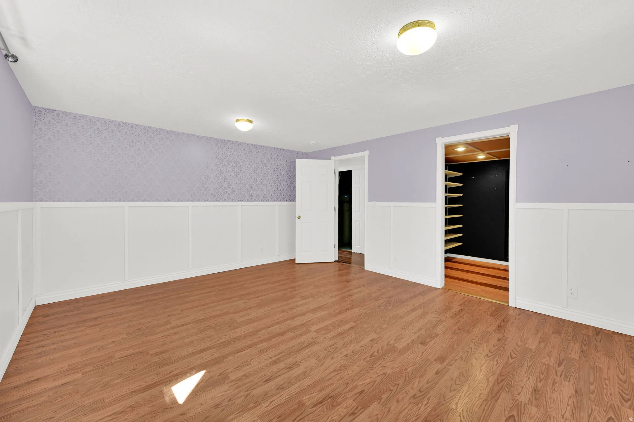 Spacious room featuring wood-finish flooring, white wainscoting, and patterned accent walls
