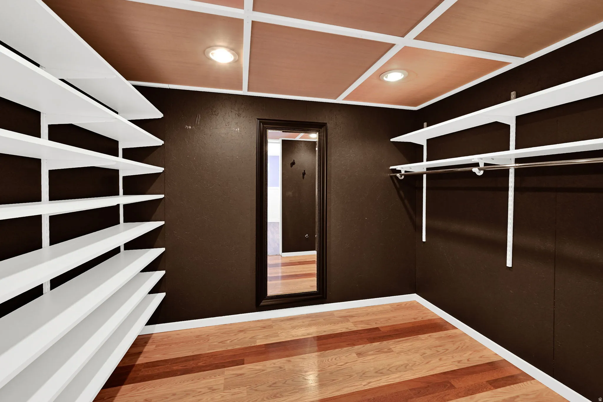 Walk-in closet featuring wood-finish flooring, dark-toned walls, and a coffered ceiling with recessed lighting