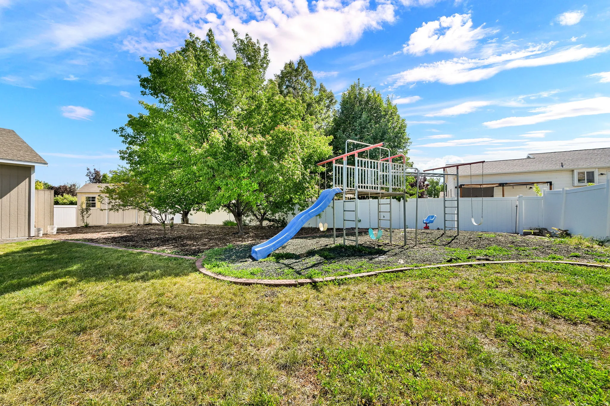 Expansive backyard with a play structure, mature trees, and a wooden storage shed