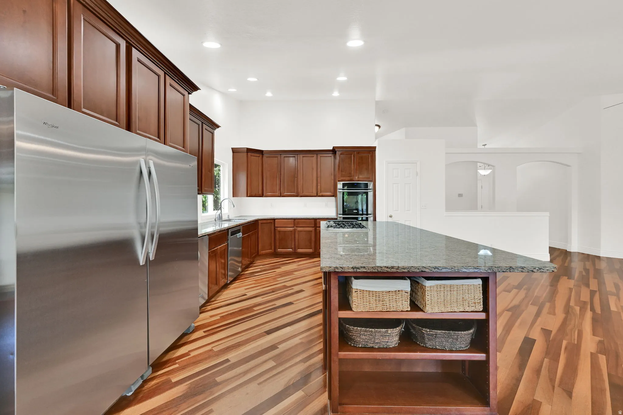 Kitchen featuring an expansive center island with countertop seating, rich wood cabinetry, stainless steel appliances, modern recessed lighting, and wood-finish flooring