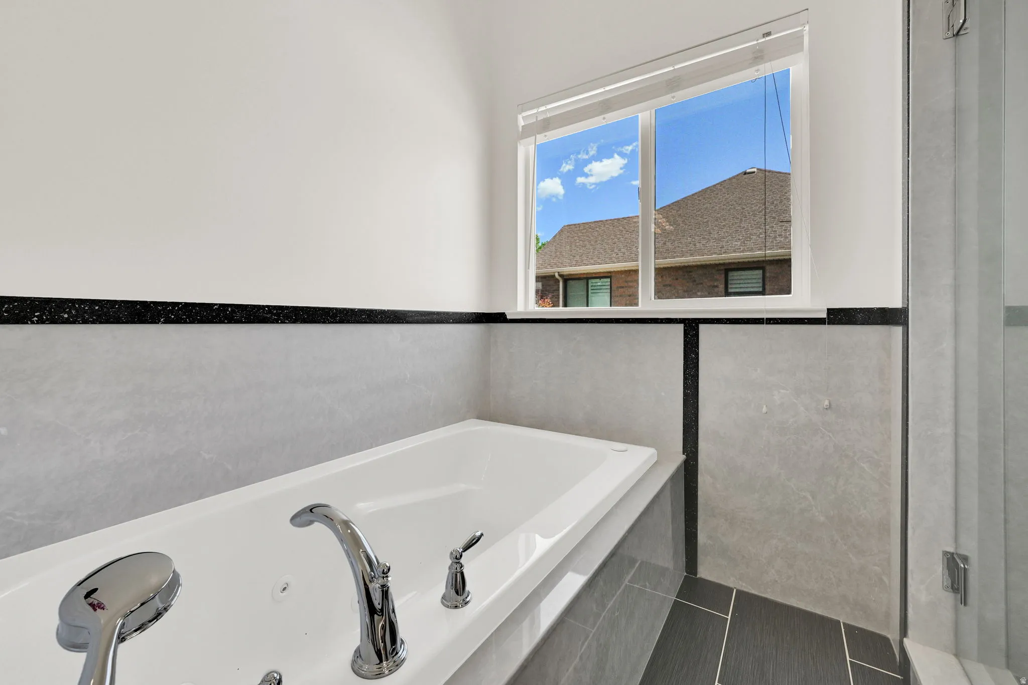 Soaking tub featuring chrome fixtures, light-toned wall tile, and black accent trim