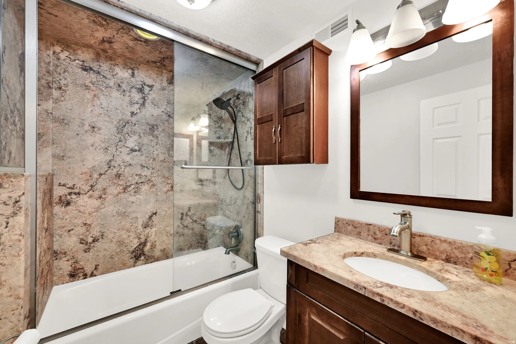 Bathroom featuring a full vanity with an integrated sink, stone-look countertop, and dark wood-finish cabinetry