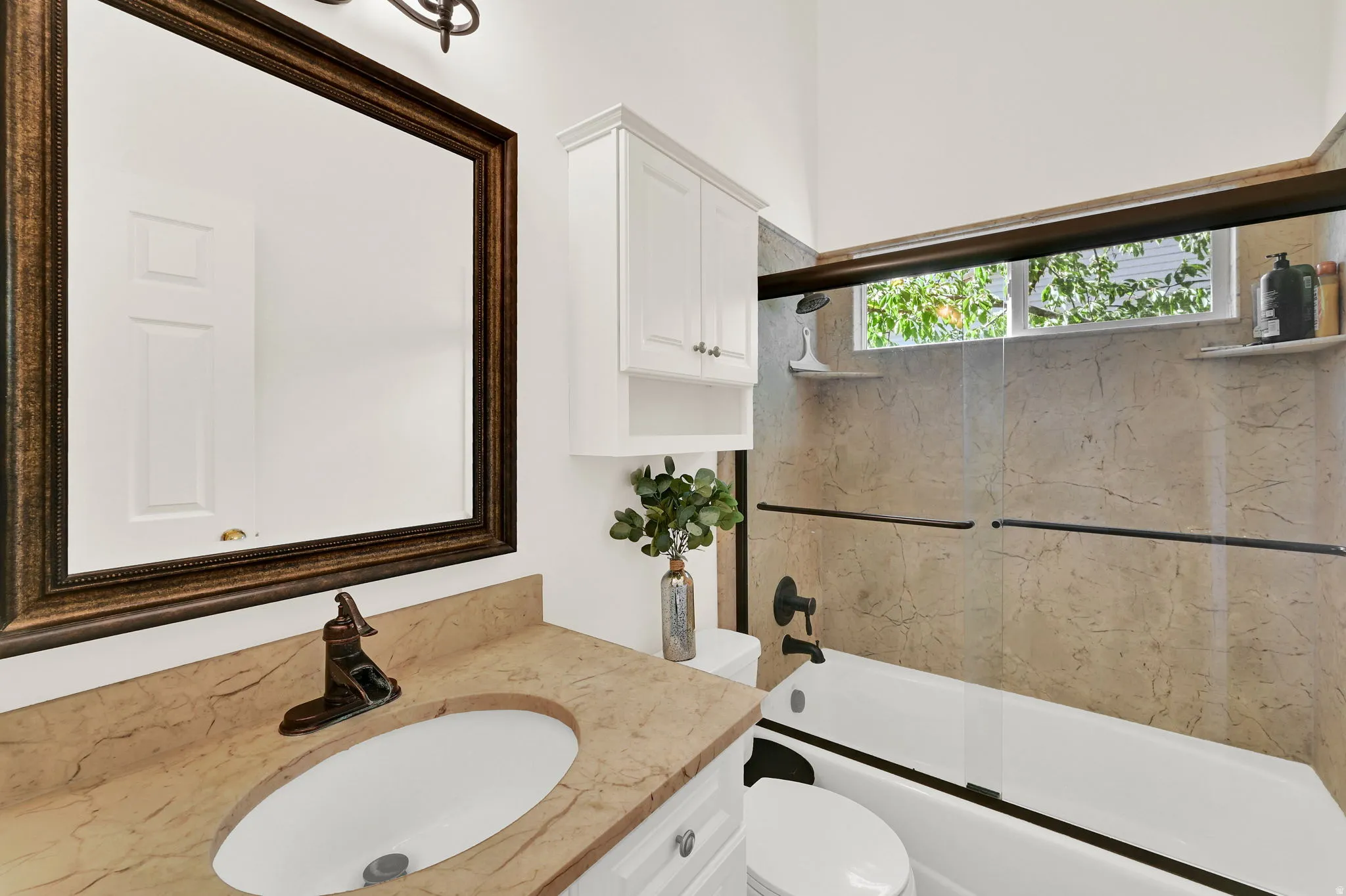 Bathroom featuring a framed vanity mirror, single basin sink with bronze-finish faucet, and white cabinetry