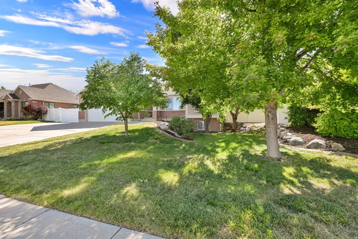 Front yard featuring mature trees, landscaped rock beds, and a manicured lawn