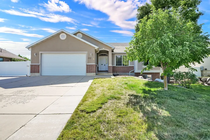Single-story stucco residence featuring a two-car garage, brick accents, and an arched entry with a decorative sidelight