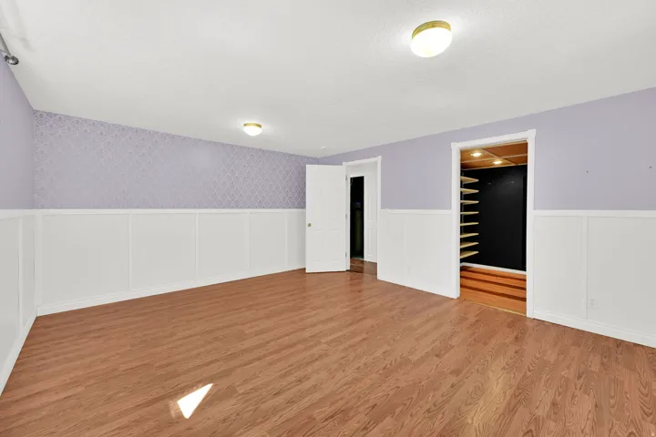 Spacious room featuring wood-finish flooring, white wainscoting, and patterned accent walls