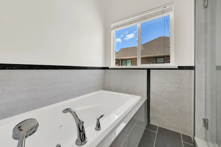 Soaking tub featuring chrome fixtures, light-toned wall tile, and black accent trim