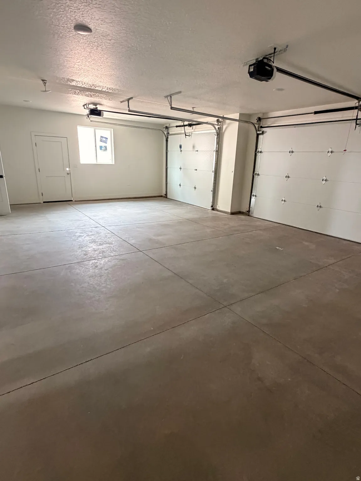 Spacious two-car garage featuring a concrete floor, two automatic garage door openers, and an interior access door