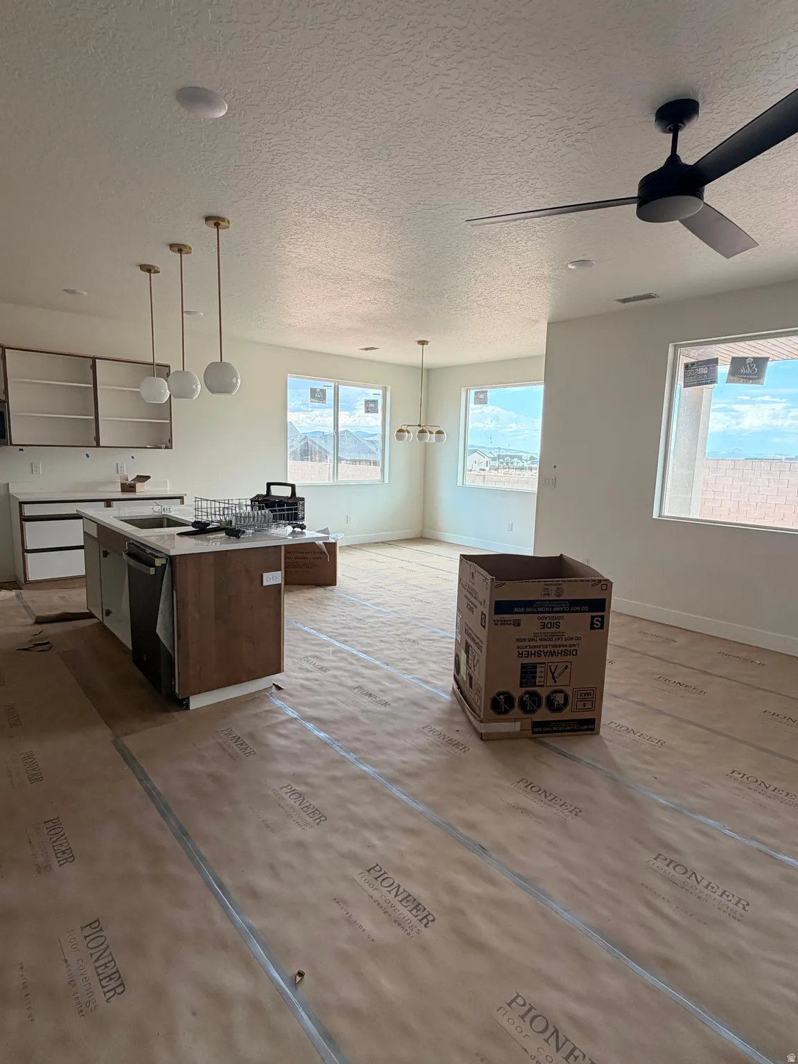 Open-concept living space featuring a kitchen island, recessed lighting, contemporary pendant fixtures, a modern ceiling fan, and multiple windows