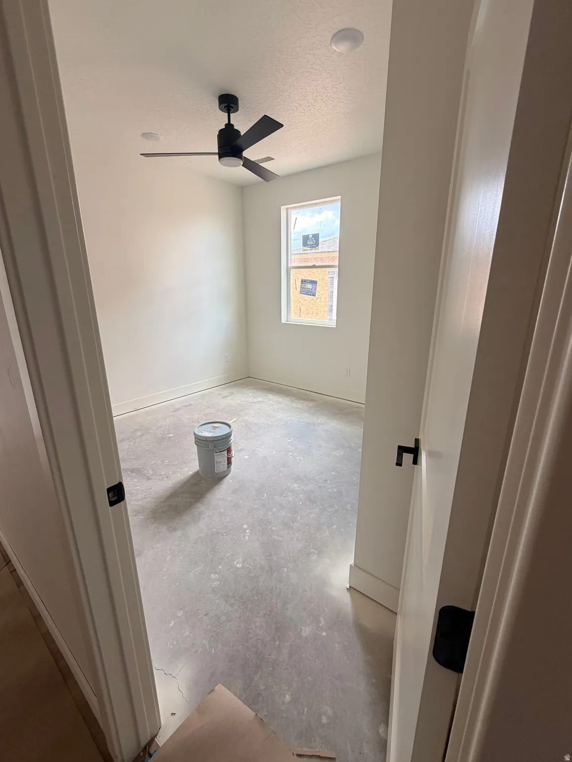 Room featuring a modern black ceiling fan with integrated lighting, a single window, white baseboards, and a contemporary door with black hardware
